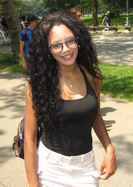 May standing in a park. She's smiling and wearing a black top and white pants.